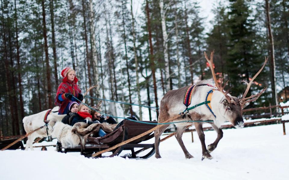 A woman in traditional Laplander costume rides with a group of tourists on a reindeer sled in the "Santa Claus Village" near Rovaniemi - JONATHAN NACKSTRAND/AFP via Getty Images