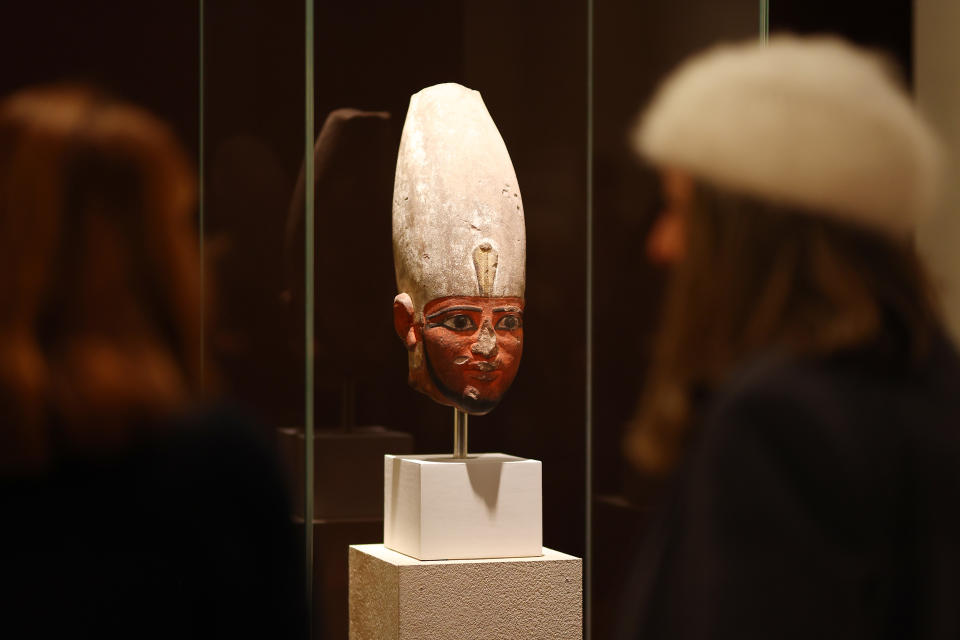 Two people view an ancient Egyptian bust displayed in a glass case at a museum