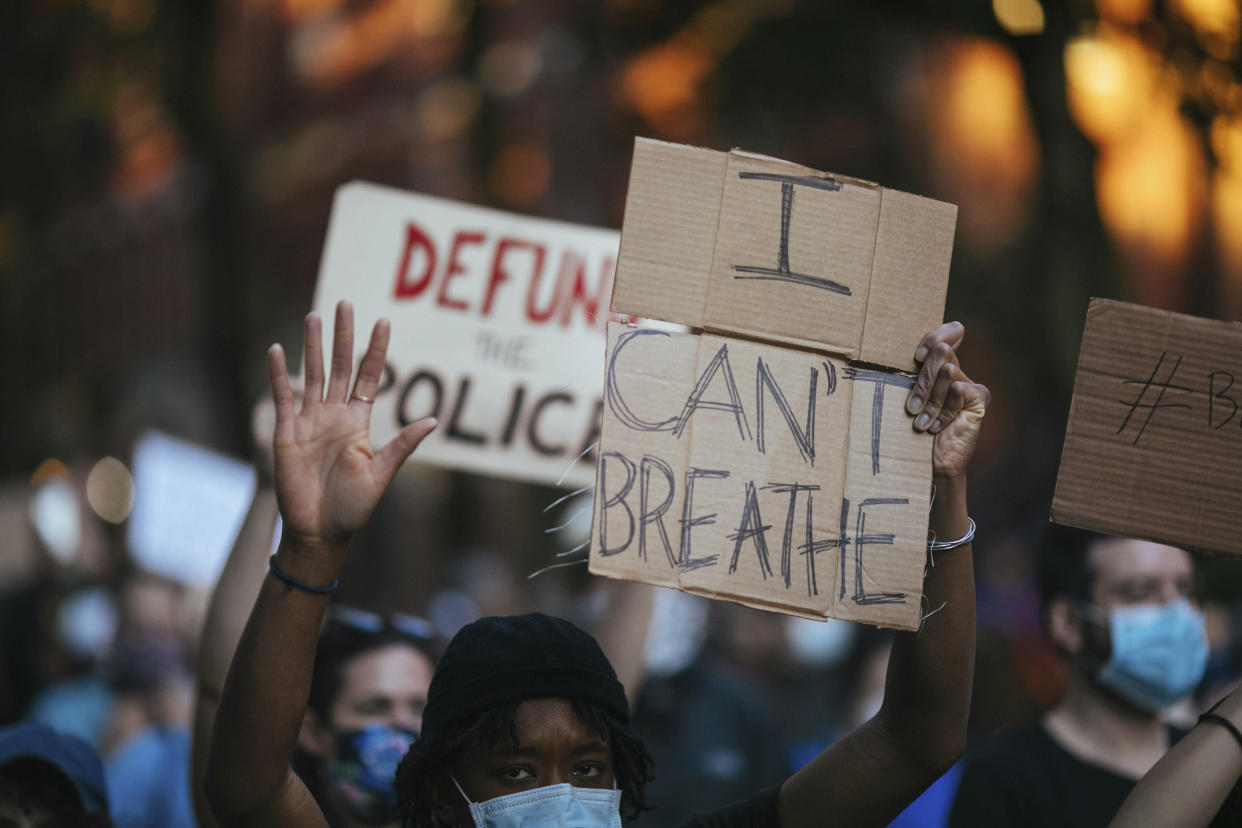 Activists carry protest signs reading: I can't breathe and Defund the police.