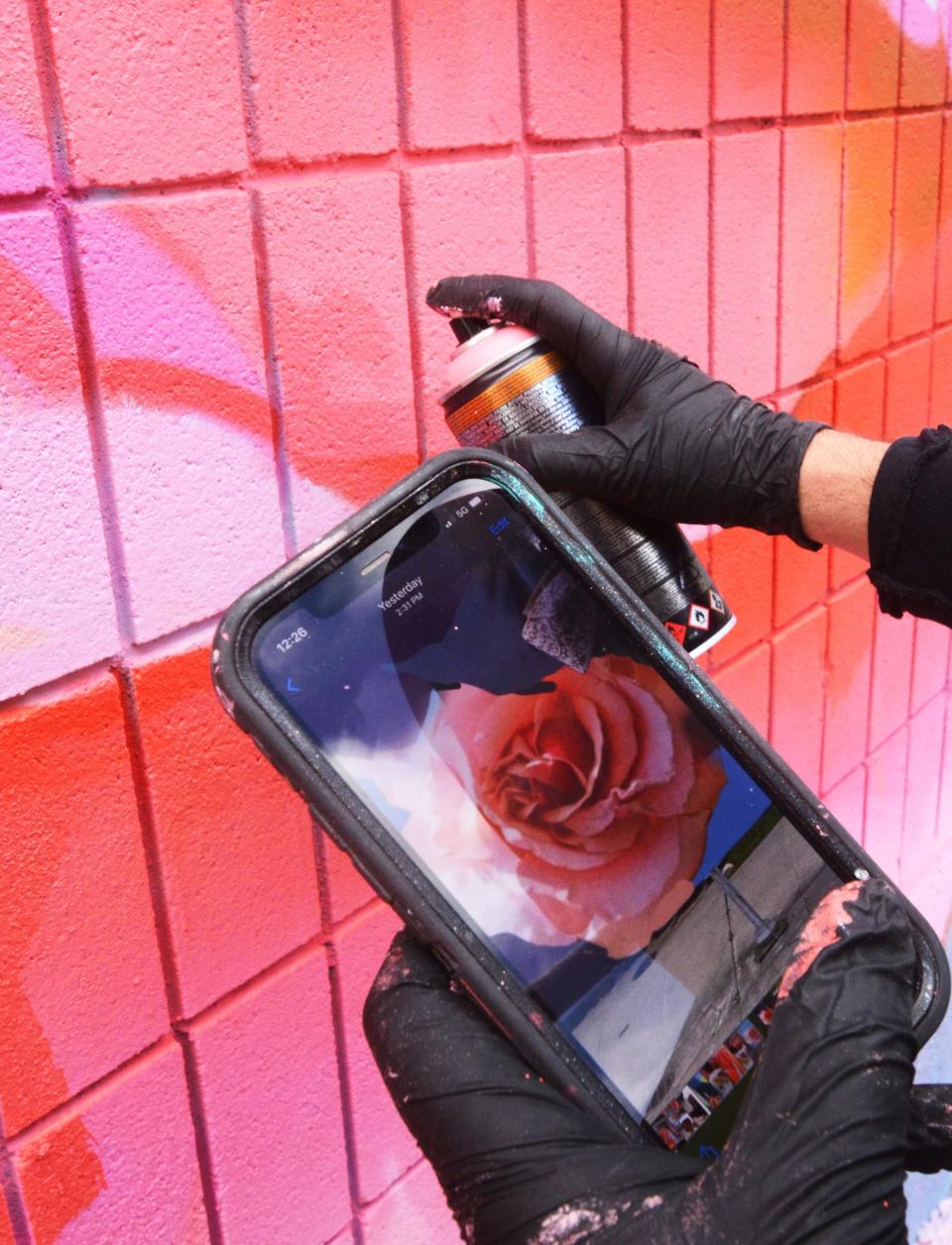 Mural artist Ben Keller uses a portion of the final rendition on his phone to paint a rose for his mural at Castle Church in downtown Norwich Friday.