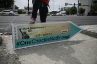 Jeremiah Miller, 17, of Atlanta, leans on a large check sign for the #OneCheckIsNotEnough campaign near Georgia Senator David Perdue's office on Tuesday, Aug. 11, 2020, in Atlanta. The campaign said the large check is to urge politicians to support recurring direct payments in the next coronavirus relief package. (AP Photo/Brynn Anderson)