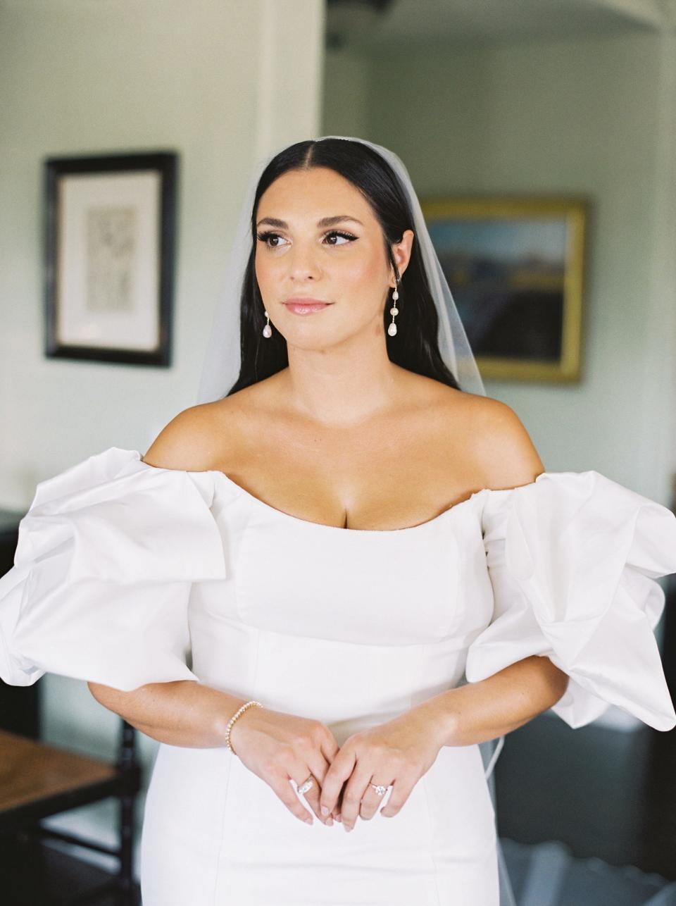 A bride stands with her hands folded in her wedding dress.