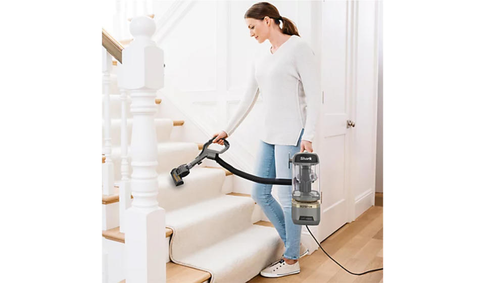 Woman using handheld head with one hand and holding the canister pod in another to tackle the carpeted stairs. 