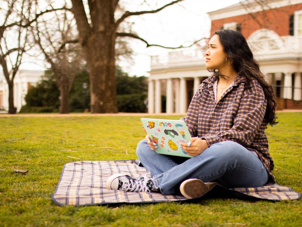 Mary Kurbanov sitting on a blanket on a lawn with a laptop in her lap