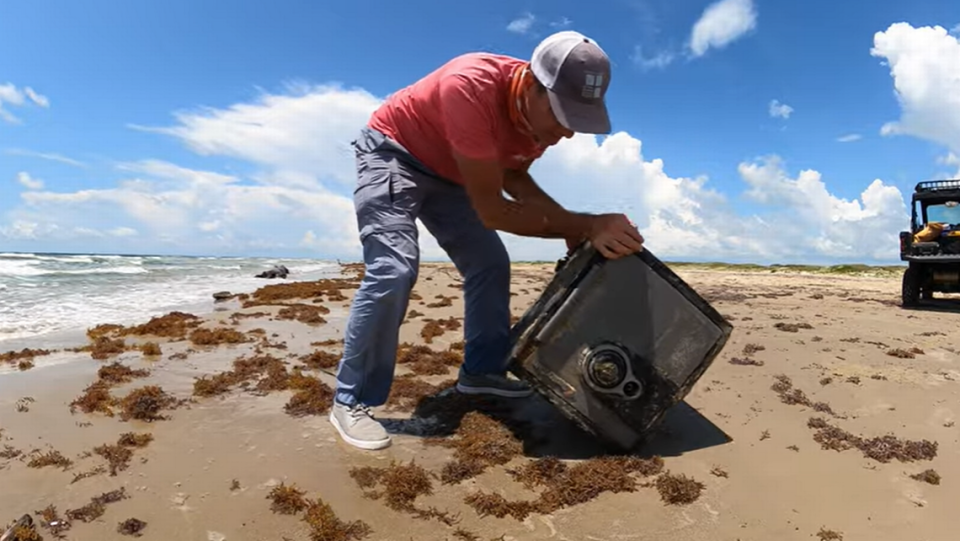 Jace Tunnell moves the safe around on the beach, testing its weight and listening for any objects inside.