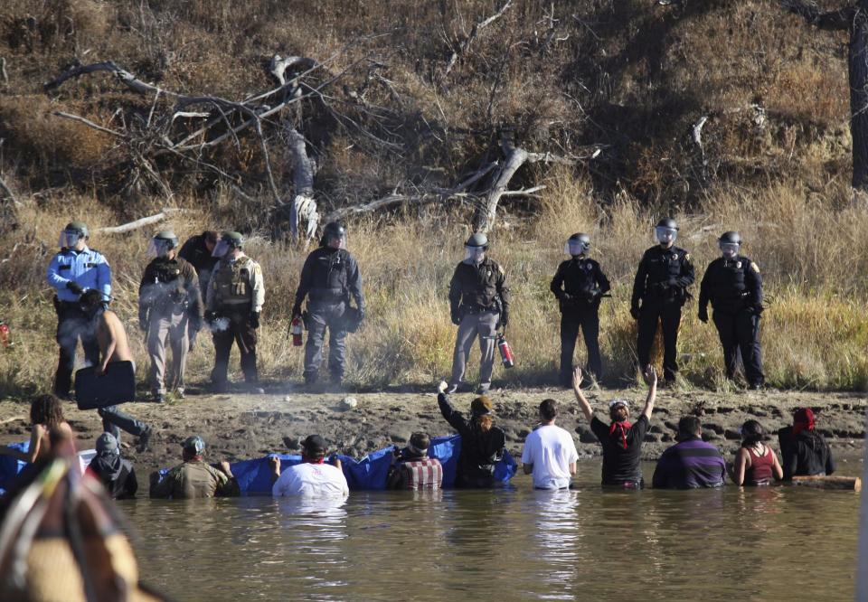 FILE - In this Nov. 2, 2016, file photo, protesters demonstrating against the expansion of the Dakota Access pipeline wade in cold creek waters confronting local police near Cannon Ball, N.D. North Dakota officials appear poised to go after the U.S. government — and thus U.S. taxpayers — to recoup more than $38 million in state expenses related to months of protests against the Dakota Access pipeline. (AP Photo/John L. Mone, File)