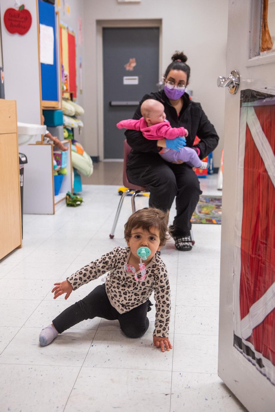 Emily Healy, 11 months old, crawls toward the door as caretaker Briana Diaz holds baby Emma Engel, 5 months old, at Victoria's Castle Daycare in New Windsor on January 21, 2022.