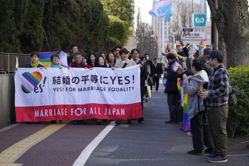 Plaintiffs holding a banner walk towards the Tokyo district court for the ruling regarding LGBTQ+ marriage rights as supporters of the LGBTQ+ community wave rainbow flags in Tokyo, Thursday, March 14, 2024. The Japanese court on Thursday ruled that not allowing same-sex couples the same marital benefits as heterosexuals violates their fundamental right to have a family, but the current civil law did not take into consideration sexual diversity and is not clearly unconstitutional, a partial victory for Japan's LGBTQ+ community calling for equal marriage rights. (AP Photo/Hiro Komae)