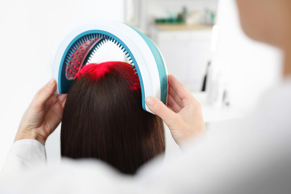 A person undergoing a light therapy treatment for hair growth, with a device emitting red light placed over their head