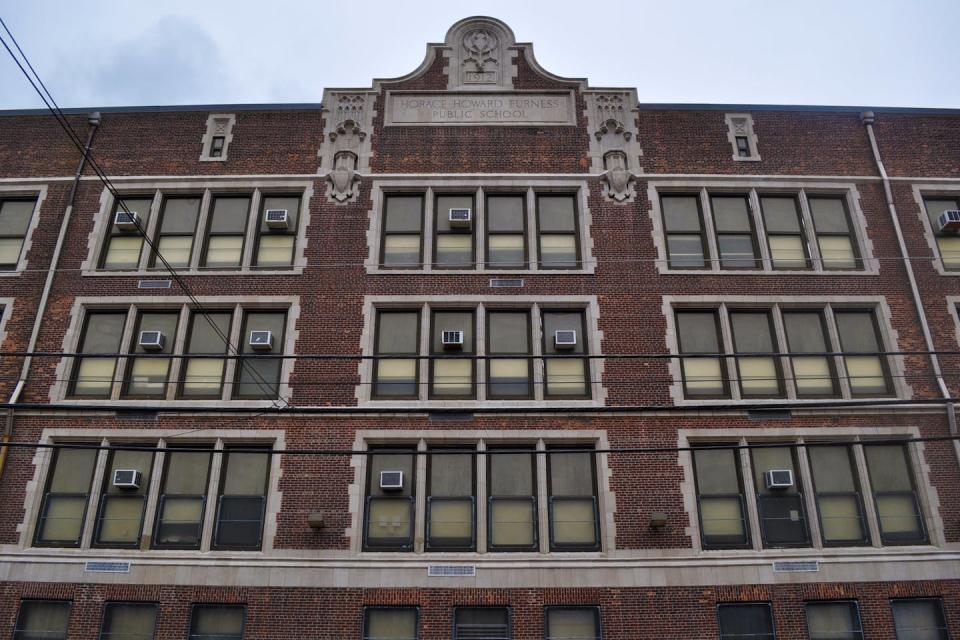 Front of a four-story brick school building with tall windows, some with air-conditioners