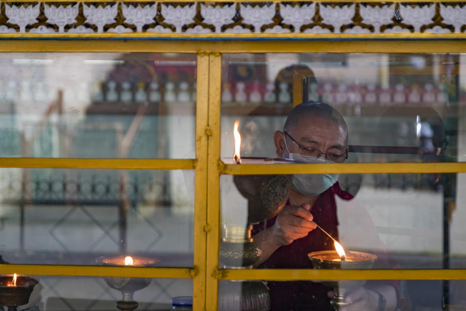 An exile Tibetan Buddhist monk wears a face mask as a precautionary measure against the coronavirus as he lights a ceremonial butter lamp in Dharmsala, India, Friday, Sept. 11, 2020. India's coronavirus cases are now the second-highest in the world and only behind the United States. (AP Photo/Ashwini Bhatia)