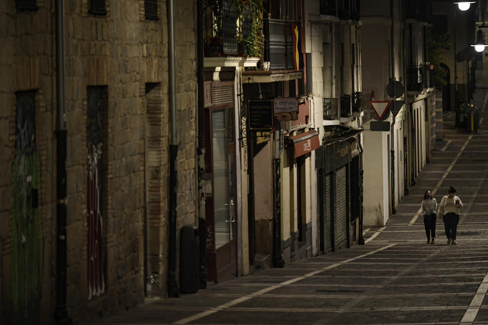 Residents wearing face mask protection as they walk along an empty Javier street, in Pamplona, northern Spain, Saturday, Oct. 24, 2020, as new measures against the coronavirus began in the Navarra province where all bar and restaurants are closed for 15 days from Wednesday midnight. (AP Photo/Alvaro Barrientos)