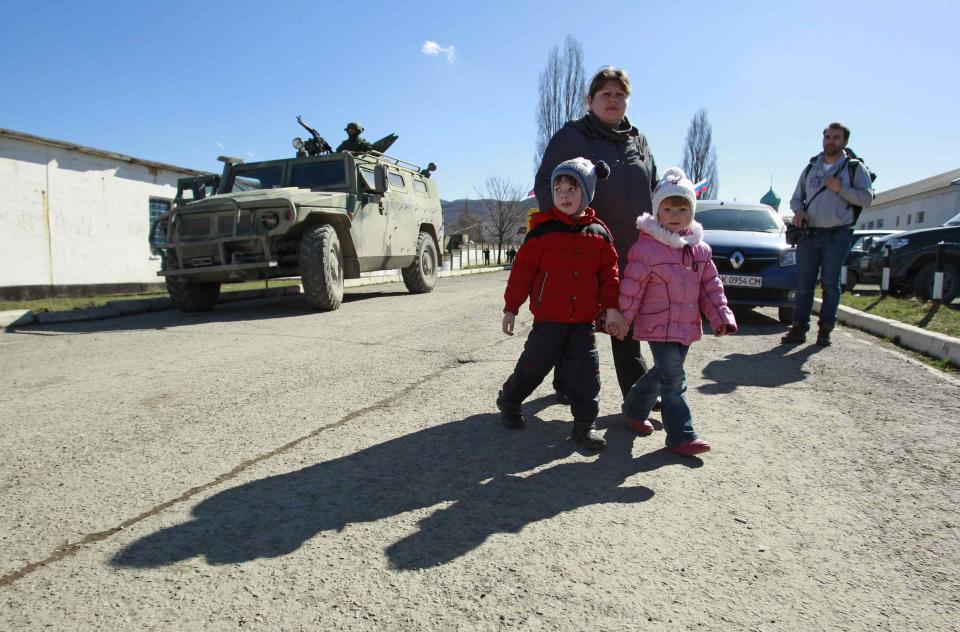 A woman with children walks by a military personnel member, believed to be a Russian serviceman, who stands guard on a military vehicle outside the territory of a Ukrainian military unit in the village of Perevalnoye outside Simferopol March 3, 2014. Ukraine mobilised for war on Sunday and Washington threatened to isolate Russia economically after President Vladimir Putin declared he had the right to invade his neighbour in Moscow's biggest confrontation with the West since the Cold War. Russian forces have already bloodlessly seized Crimea, an isolated Black Sea peninsula where Moscow has a naval base. REUTERS/David Mdzinarishvili (UKRAINE - Tags: POLITICS MILITARY CIVIL UNREST)