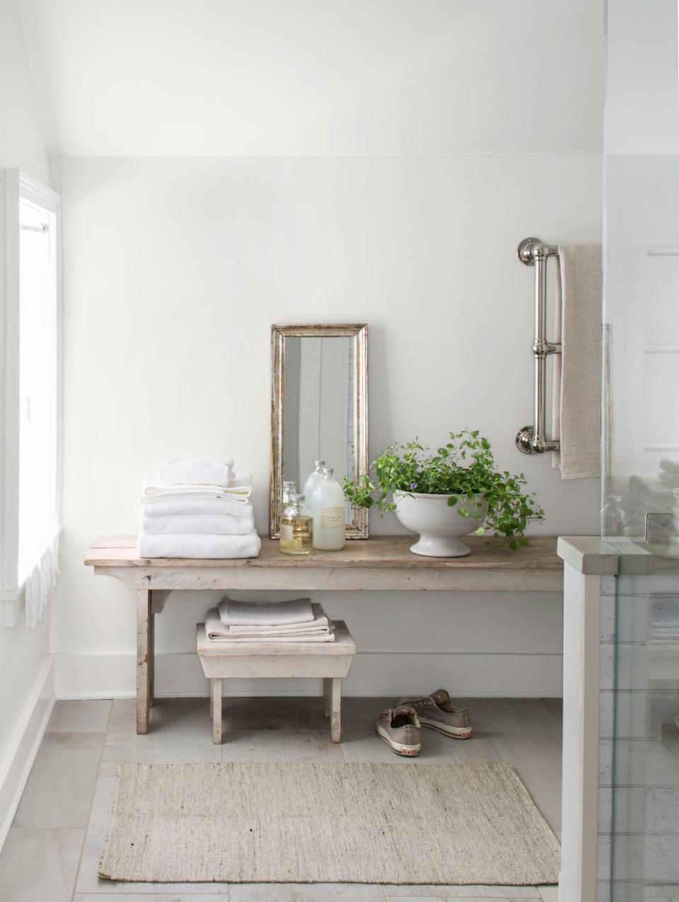 bathroom with gray tile and antique bench with towels and bath supplies on it