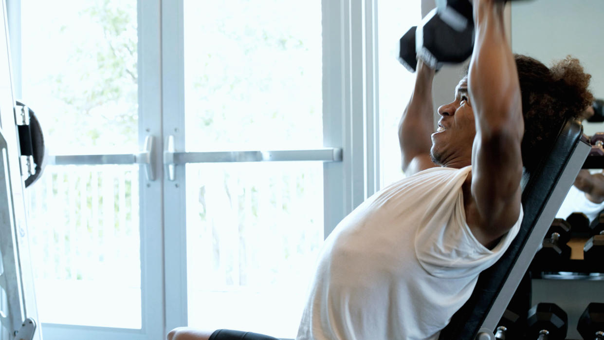  Man performs seated shoulder press with dumbbells in a gym 