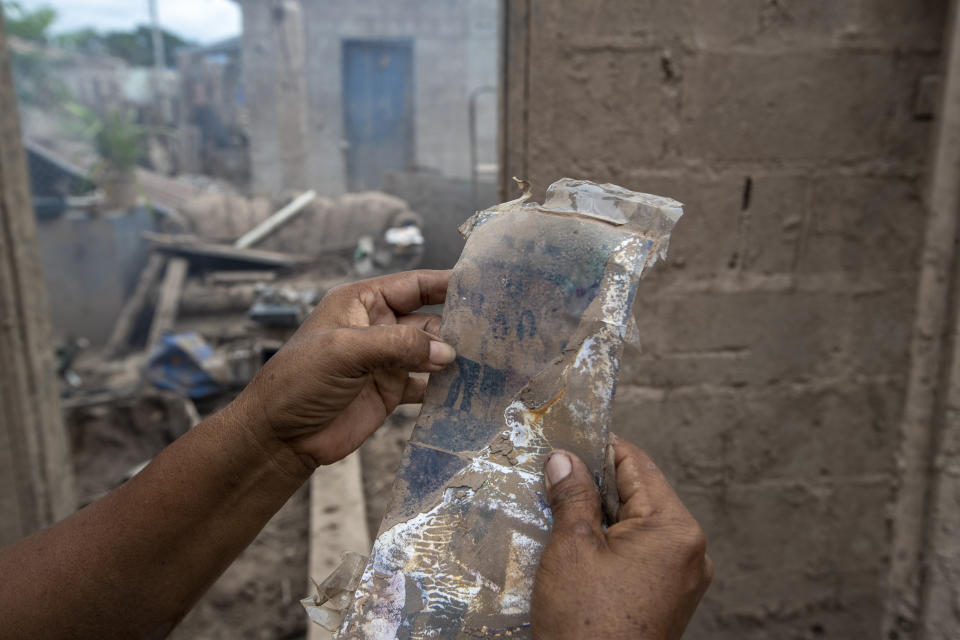 Maria Elena Vasquez shows a photo recovered from her home destroyed by last year's hurricanes Eta and Iota in La Lima, on the outskirts of San Pedro Sula, Honduras, Wednesday, Jan. 13, 2021. Vasquez returns every afternoon to remove the mud in hopes of returning to live here. (AP Photo/Moises Castillo)