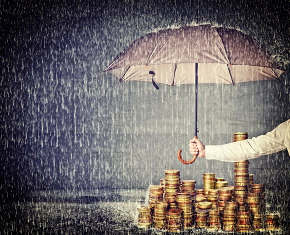 An umbrella protects a pile of gold coins from the rain.