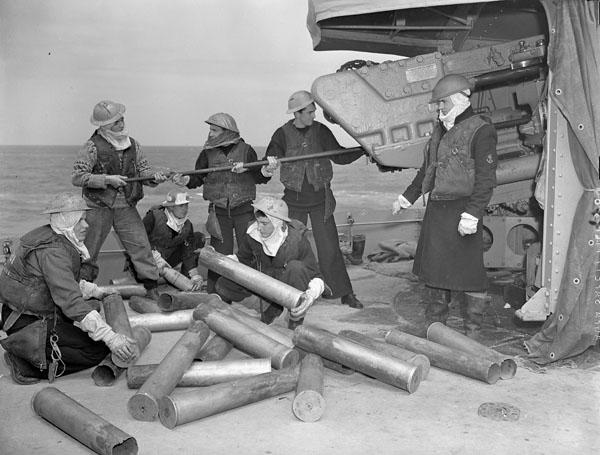 A 4.7-inch (12 cm) gun crew of the destroyer HMCS Algonquin piling shell cases and sponging out the gun after bombarding German shore defences in the Normandy beachhead.