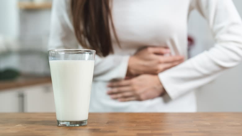 Person holding stomach with glass of milk on countertop in foreground