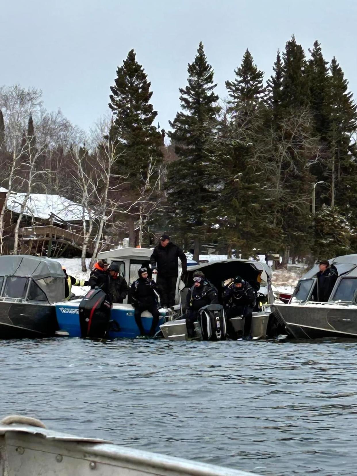 Kurt Mason and two other members of the Oogoogeek dive team sit on the edge of boats before plunging into the water to search for the body of a missing Island Lake community member.  (Submitted by Kurt Mason  - image credit)