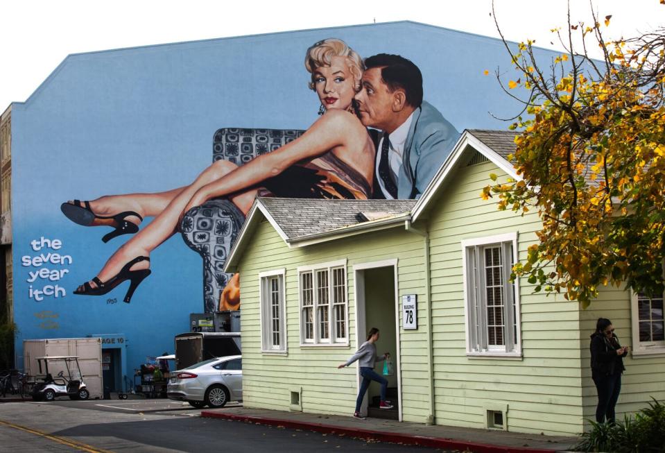 A mural of a woman and a man on a big building appears above a bungalow.