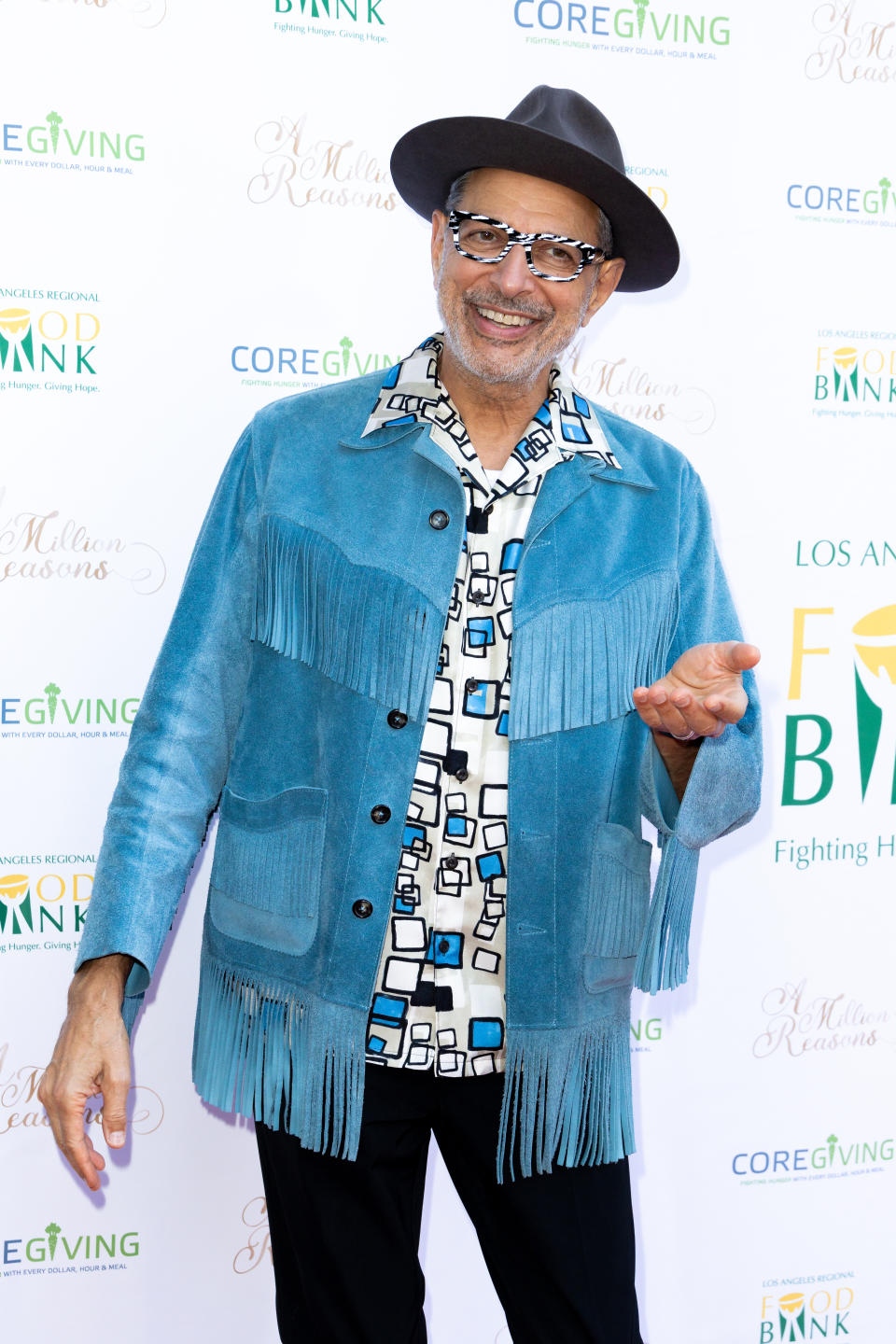 Homme dans une veste bleue à franges et un chapeau souriant lors d'un événement caritatif