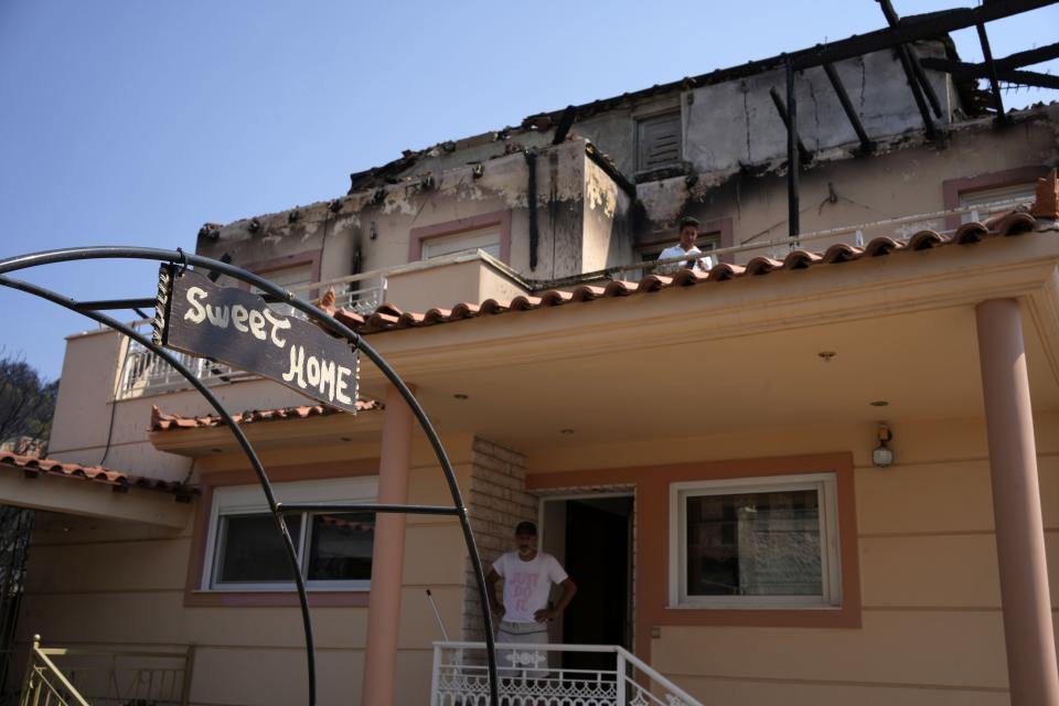 The owner of a house stands at the entrance, during a wildfire in Acharnes suburb, on Mount Parnitha, in northwestern Athens, Greece, Thursday, Aug. 24, 2023. A major wildfire burning on the northwestern fringes of the Greek capital has torched homes and is now threatening the heart of a national park of Parnitha, one of the last green areas near the Greek capital. (AP Photo/Thanassis Stavrakis)