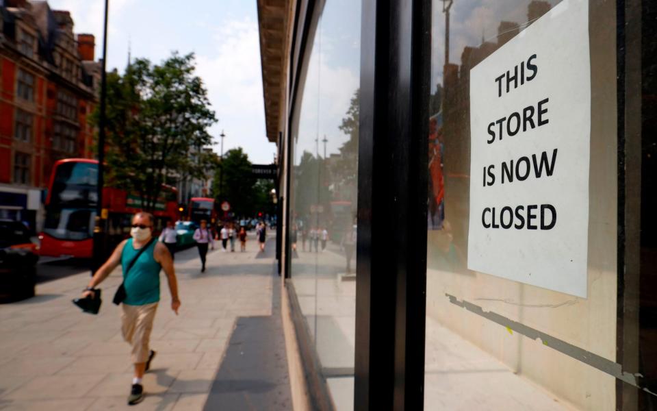 A pedestrian wearing a face mask or covering due to the COVID-19 pandemic, walks past a sign in the window of a store alerting customers that the shop has closed-down