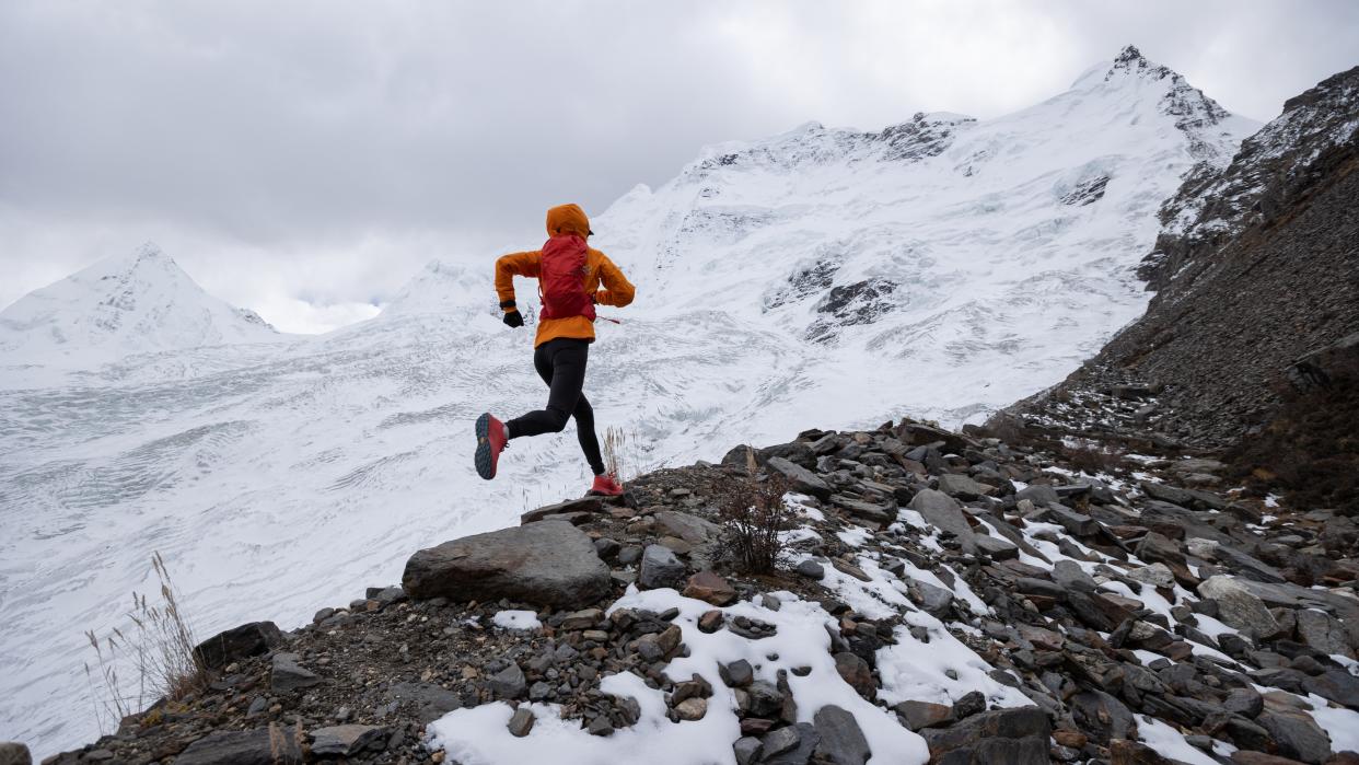  Woman trail runner cross country running up hill to winter snow mountain top. 