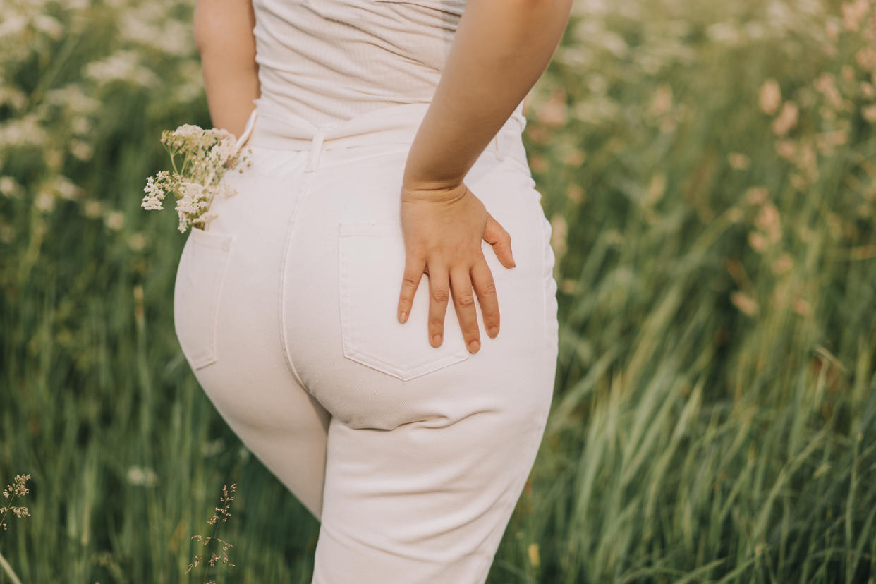 Closeup of a woman in white jeans on a blooming field background. Stylish look, fashion for curvy women, outdoor recreation.