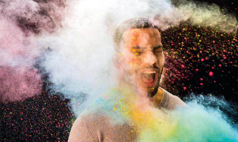 Powder paint splashing on young manColourful powder paint splashing on young man against black background.