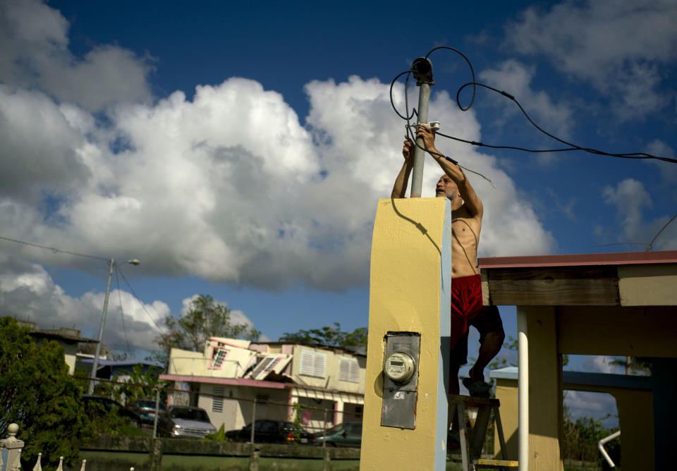 FILE - In this Oct. 13, 2017 file photo, a resident tries to connect electrical lines downed by Hurricane Maria in preparation for when electricity is restored in Toa Baja, Puerto Rico, about three weeks after the storm. Largely due to decades of neglect and years of fiscal crisis, the Puerto Rican electrical grid collapsed into the United States' longest-ever blackout after Maria hit on Sept. 20, 2017. (AP Photo/Ramon Espinosa, File)