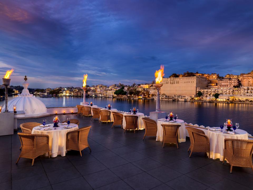 A rooftop restaurant with round tables, wicker chairs, and large torches overlooking the lake and city.