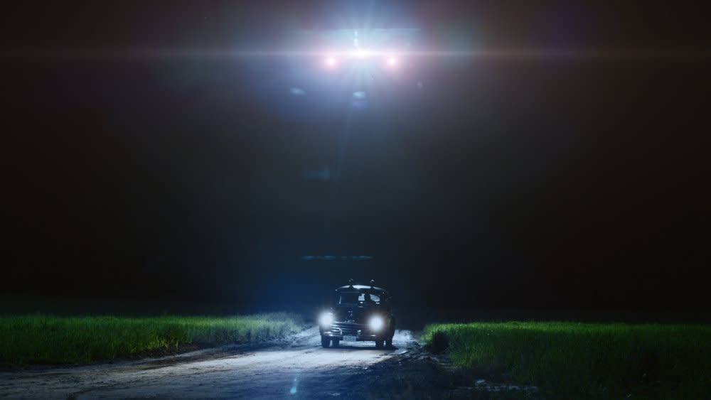  A pickup truck in a field at night, with the bright lights of a strange craft above it. 