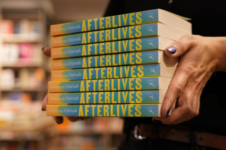 A member of staff holds a pile of copies of "Afterlives" by Zanzibar-born novelist Abdulrazak Gurnah in a book shop in London, Thursday, Oct. 7, 2021. U.K.-based Tanzanian writer Abdulrazak Gurnah, whose experience of crossing continents and cultures has fed his novels about the impact of migration on individuals and societies, won the Nobel Prize for Literature on Thursday. (AP Photo/Alberto Pezzali)