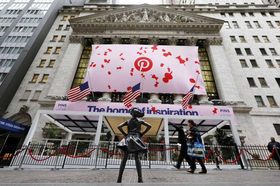 The statue of the "Fearless Girl" looks toward the facade of the New York Stock Exchange decorated for the Pinterest IPO, Thursday, April 18, 2019. (AP Photo/Richard Drew)