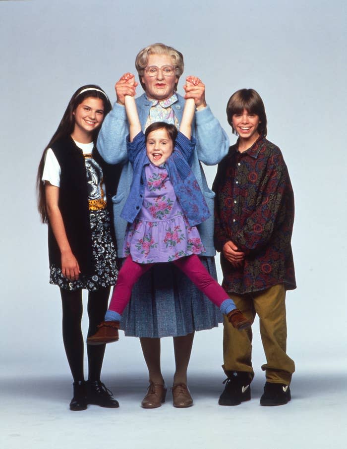 Promotional image of 'Mrs. Doubtfire' characters posing together, with actor in elderly woman disguise center