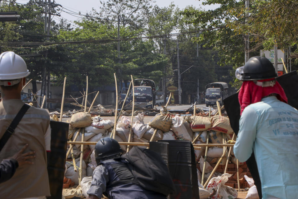 Anti-coup protesters take cover behind makshift barricades as trucks with riot policemen arrive in Yangon, Myanmar Thursday, March 11, 2021. (AP Photo)