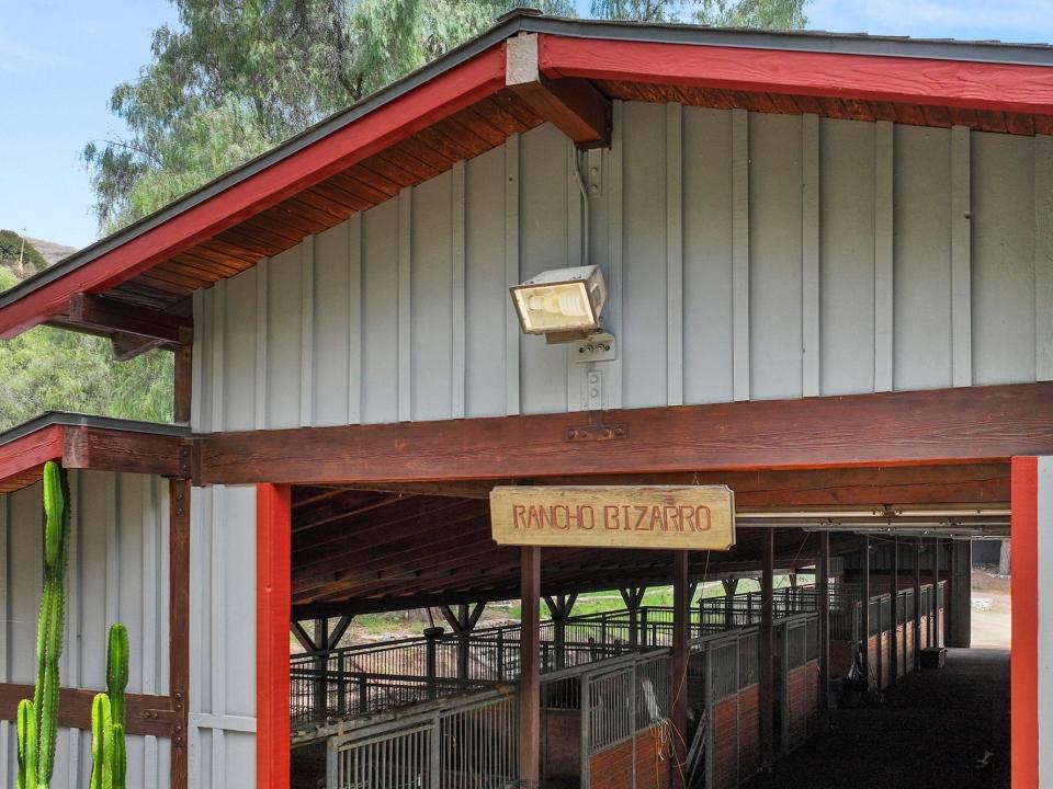 A red and gray horse barn with the doors open and a wooden sign that says rancho bizarro