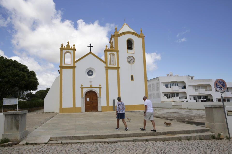 A couple walk in front of the church in Praia da Luz, in Portugal's Algarve coast, Thursday, June 4, 2020. German police have identified a 43-year-old imprisoned German citizen as a suspect in the 2007 disappearance in Praia da Luz of British girl Madeleine McCann. (AP Photo/Armando Franca)