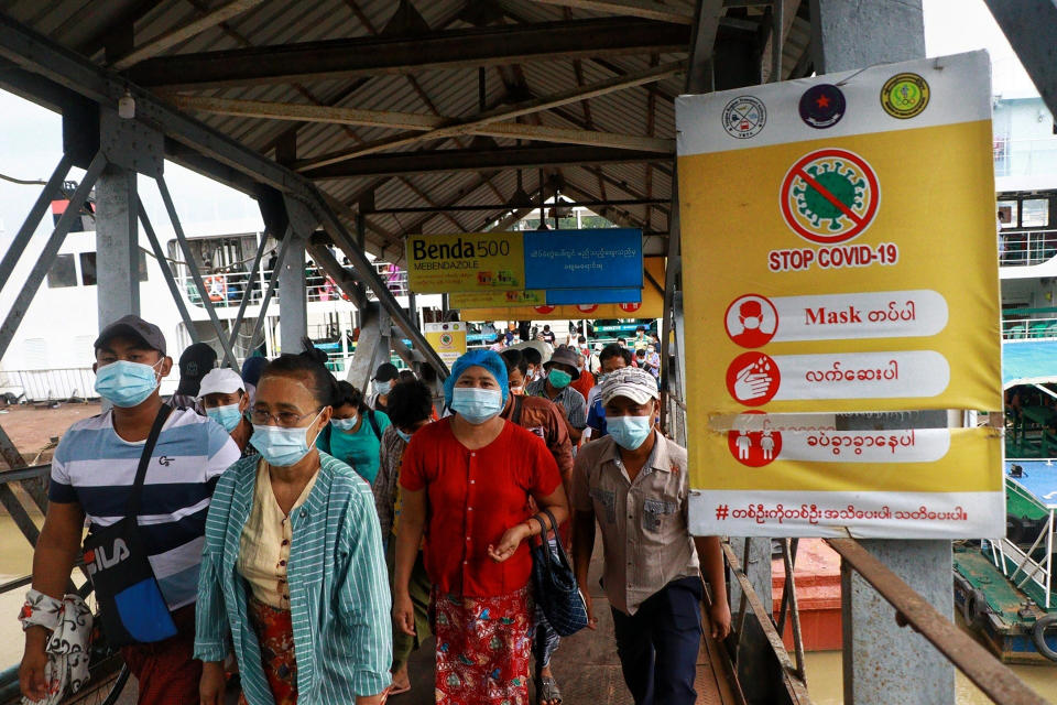 FILE - In this July 27, 2021, file photo, ferry passengers wearing face masks to help curb the spread of the coronavirus walk past a "Stop COVID-19" poster at the Pansodan jetty in Yangon, Myanmar. With coronavirus deaths rising in Myanmar, there are growing allegations from residents and human rights activists that the military government, which seized control in February, is using the pandemic to consolidate power and crush opposition. (AP Photo, File)