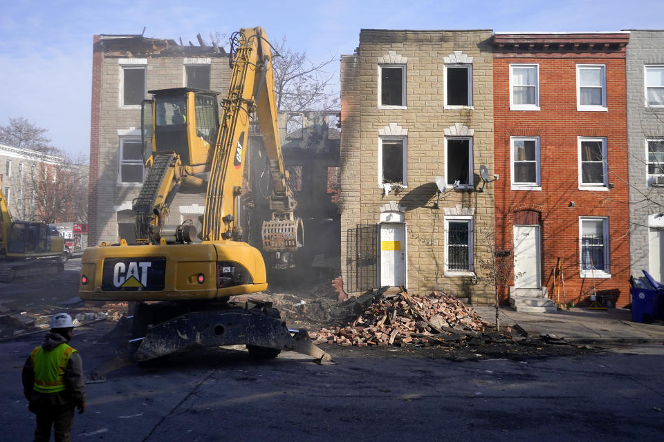 An excavator is used to pull debris off a building during efforts to retrieve the body of a deceased firefighter caught in the building's collapse while battling a two-alarm fire in the vacant row home, Monday, Jan. 24, 2022, in Baltimore. Officials said several firefighters died during the blaze. (AP Photo/Julio Cortez)