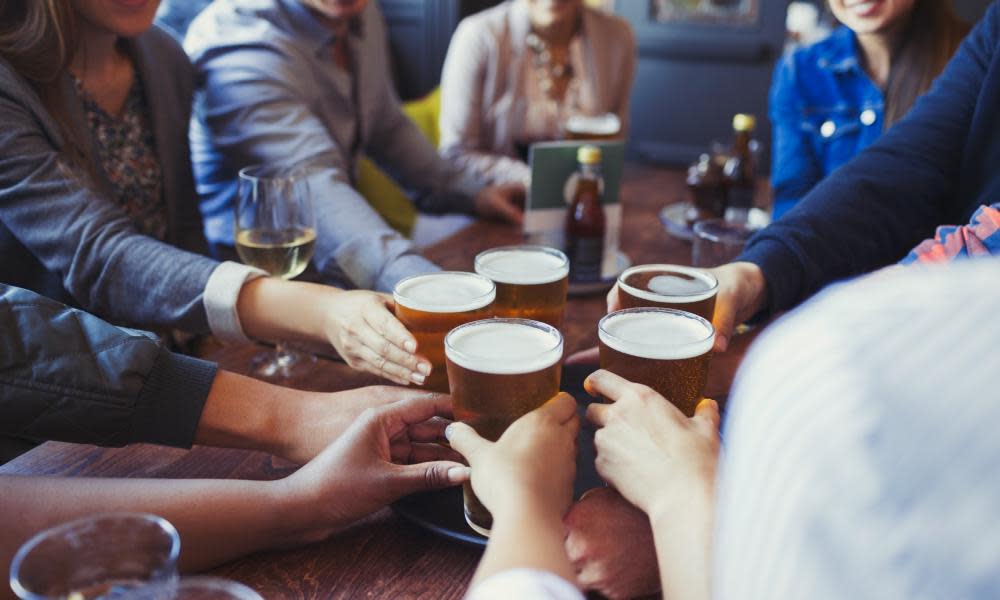 Friends reaching for beer glasses on a bar table.