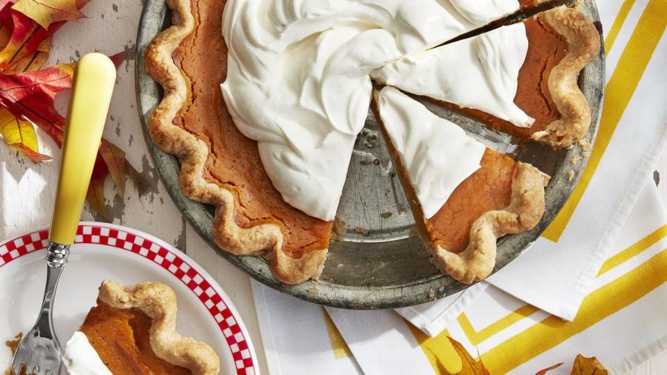 gingery sweet potato pie topped with whipped cream in a metal pie dish with a slice on a plate next to it