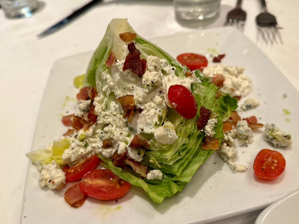 wedge of lettuce with cheese, cherry tomatoes, bacon pieces on square white plate