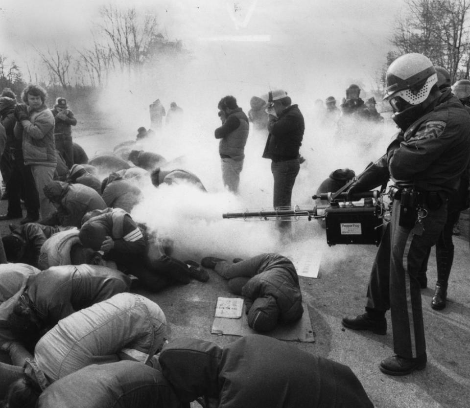 A town policeman sprays pepper gas on striking Brown & Sharpe workers on March 23, 1982, on a picket line in North Kingstown. Earlier, pickets had stoned the vehicles of those going to work.