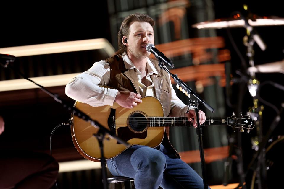 morgan wallen playing guitar and singing while sitting on a stool for a stage performance