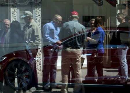 People are reflected in the dealership windows as they wait in line at a Tesla Motors store to place deposits on the electric car company's mid-priced Model 3 in La Jolla, California, March 31, 2016. REUTERS/Mike Blake