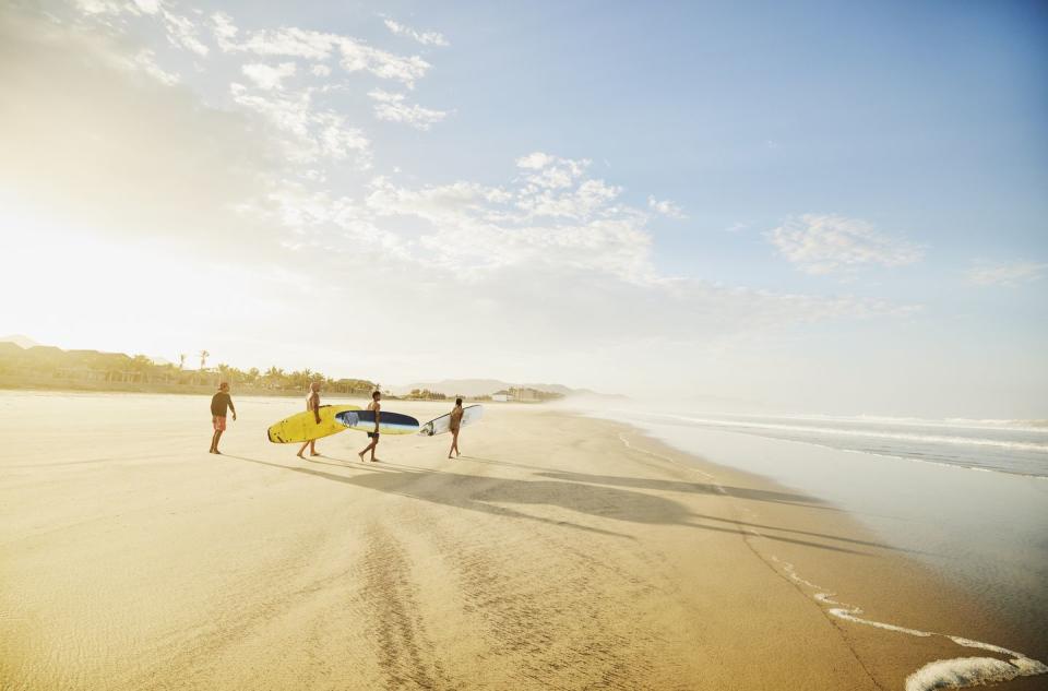 extreme wide shot of family carrying surfboards on tropical beach while taking surf lesson during vacation