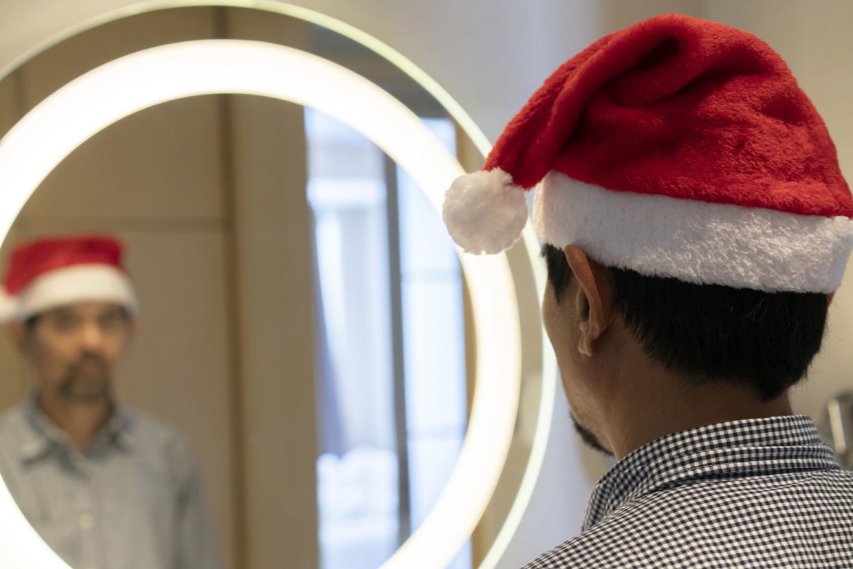 man in Santa hat looking in mirror solemnly